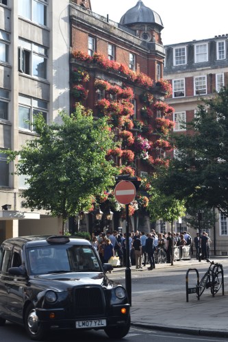Cette photo résume à elle seule la ville : taxi typiquement londonien, gerbes de fleurs accrochées aux fenêtres et collègues de travail fêtant leur début de week-end en prenant un verre au bar du coin.